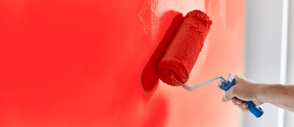 Une personne peint un mur intérieur avec un rouleau à peinture, appliquant une peinture rouge vif sur une surface blanche