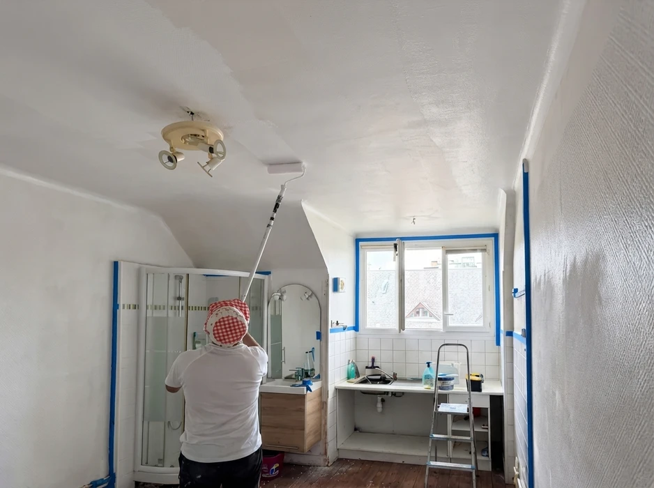 Peintre ou bâtisseur peint un mur blanc sur une échelle à l'aide d'un rouleau en gros plan regardant loin pendant qu'il travaille