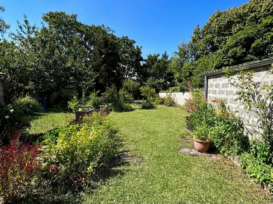 Jardin résidentiel avec pelouse verte entretenue, massifs de fleurs colorées incluant bougainvilliers roses, plantations en bacs et bordures paysagères
