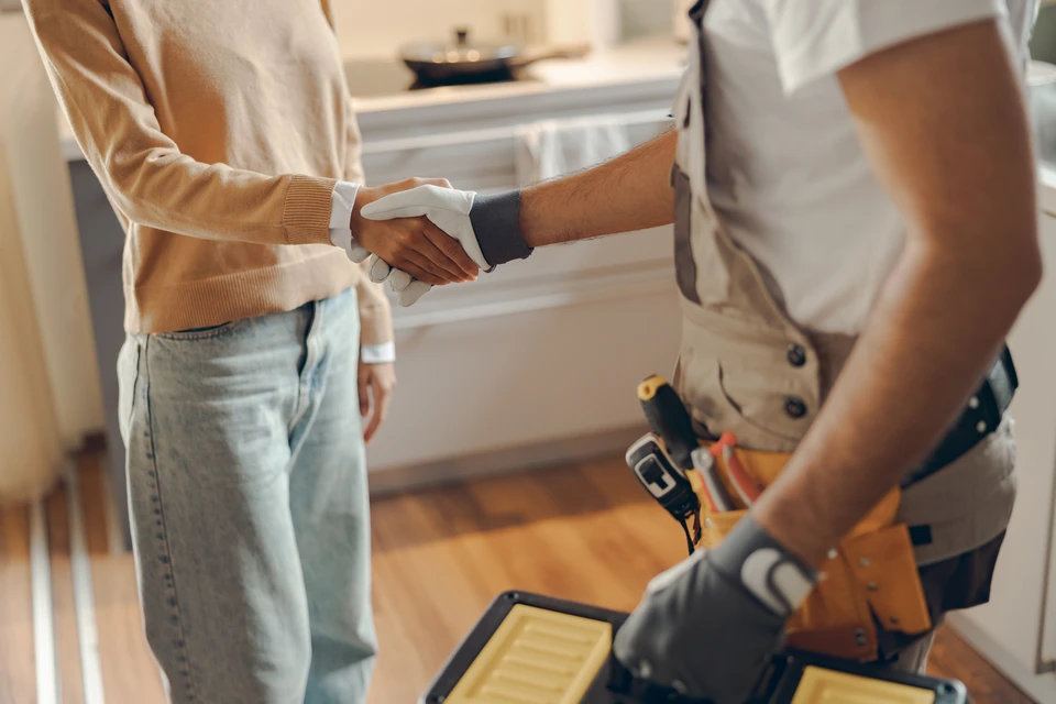 Un artisan en chemise en jean installe des éléments de cuisine blanche moderne dans un intérieur contemporain aux murs blancs
