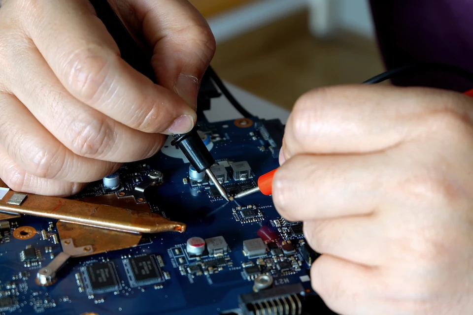 Un technicien informatique travaillant chez un client, assis à un bureau domestique, intervenant sur un ordinateur personnel. L'environnement doit être celui d'une maison ou d'un petit bureau résidentiel avec mobilier courant. Le technicien porte des vêtements professionnels simples et utilise des outils de diagnostic informatique standards. L'image doit transmettre la confiance, la proximité et l'accessibilité du service à domicile.